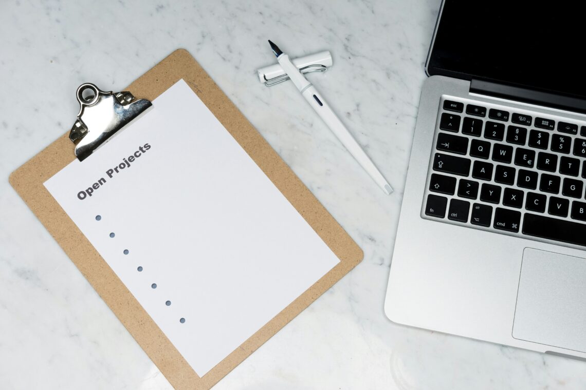 Clipboard with an 'Open Projects' checklist, pen and laptop on a marble desk, representing business admin and project tracking.