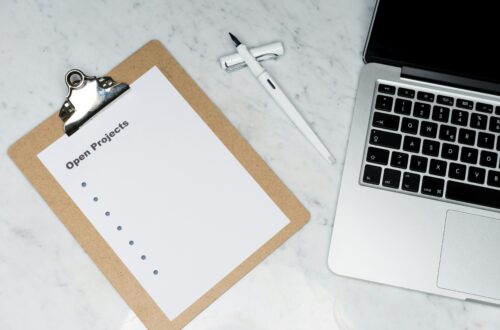 Clipboard with an 'Open Projects' checklist, pen and laptop on a marble desk, representing business admin and project tracking.