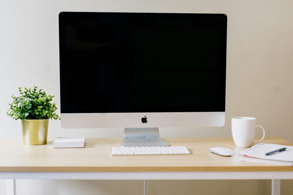 Clean, minimal desk setup with an iMac, notebook, mug and plant, showing an organised and approachable virtual assistant workspace.